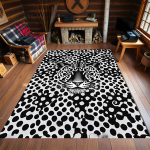 May include: A black and white area rug featuring a leopard's face. The rug has a spotted pattern with a detailed illustration of the leopard's face in the center. The rug is rectangular and placed on a wooden floor.