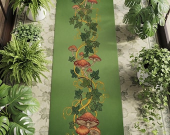 Könnte beinhalten: Eine grüne, rechteckige Yogamatte mit einem Design aus orangefarbenen Pilzen und grünem Efeu. Das Design ist auf der Matte zentriert, mit einem einfarbigen grünen Hintergrund. Die Matte ist von Topfpflanzen umgeben. Maße in Zentimetern.