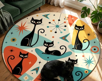 May include: A round area rug with a mid-century modern design featuring black cat illustrations on a cream background. The rug has a retro color palette of teal, orange, and yellow. A real black cat is lying on the rug.