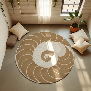 May include: A circular rug with a nautilus shell design. The rug has a spiral pattern in shades of tan, cream, and white, with a white border. The rug is on a grey floor, with cushions and a potted plant nearby.