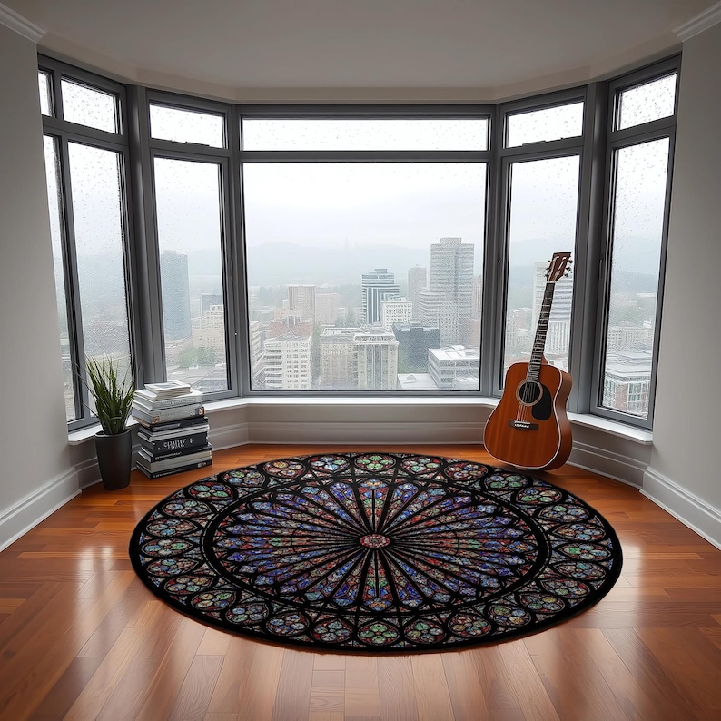 K&ouml;nnte beinhalten: Ein runder Teppich mit einem Buntglasfenster-Design in Blau-, Rot-, Gr&uuml;n- und Lilat&ouml;nen. Der Teppich liegt auf einem Holzboden vor einem gro&szlig;en Fenster mit Blick auf die Stadt. Eine Gitarre lehnt am Fenster.