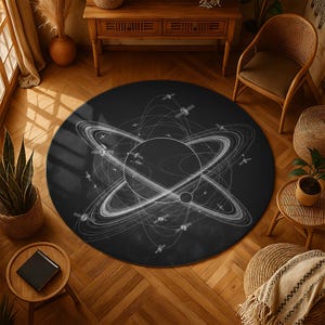 Puede incluir: Una alfombra redonda negra con un diseño gráfico blanco de un planeta rodeado de satélites en órbita. La alfombra está colocada sobre un suelo de madera, con muebles de madera y plantas en el fondo.
