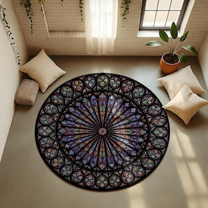 K&ouml;nnte beinhalten: Ein runder Teppich mit einem Buntglasfenster-Design. Der Teppich hat einen schwarzen Rand und ein farbenfrohes, detailliertes Muster in Blau, Rot, Gr&uuml;n und Gelb. Er liegt auf einem hellgrauen Boden, mit Kissen und einer Pflanze im Hintergrund.