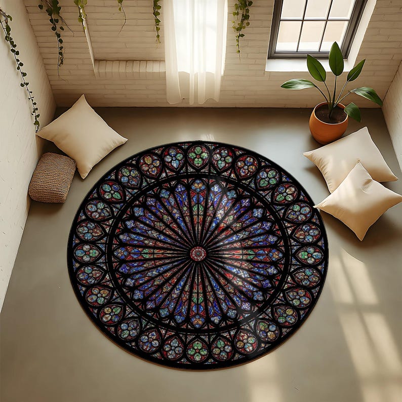 K&ouml;nnte beinhalten: Ein runder Teppich mit einem Buntglasfenster-Design. Der Teppich hat einen schwarzen Rand und ein farbenfrohes, detailliertes Muster in Blau, Rot, Gr&uuml;n und Gelb. Er liegt auf einem hellgrauen Boden, mit Kissen und einer Pflanze im Hintergrund.