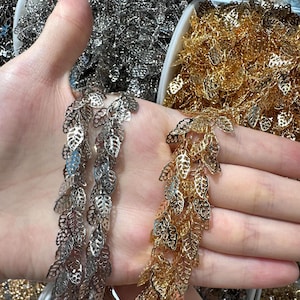 Op de afbeelding: Close-up van zilveren en gouden metalen sierranden in de vorm van bladeren. De zilveren rand is links en de gouden rand is rechts. De bladeren zijn ingewikkeld uitgesneden en de rand wordt waarschijnlijk gebruikt voor versieringen of knutselwerk.