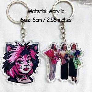 May include: Two acrylic keychains. One features a cartoon cat with pink and black hair, the other shows three people holding bouquets. The keychains are 2.56 inches in size and made of acrylic.