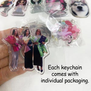 May include: Clear acrylic keychains featuring images of people holding bouquets and a diploma. The keychains are packaged individually. Other keychains with cartoon characters and a dog are visible in the background.