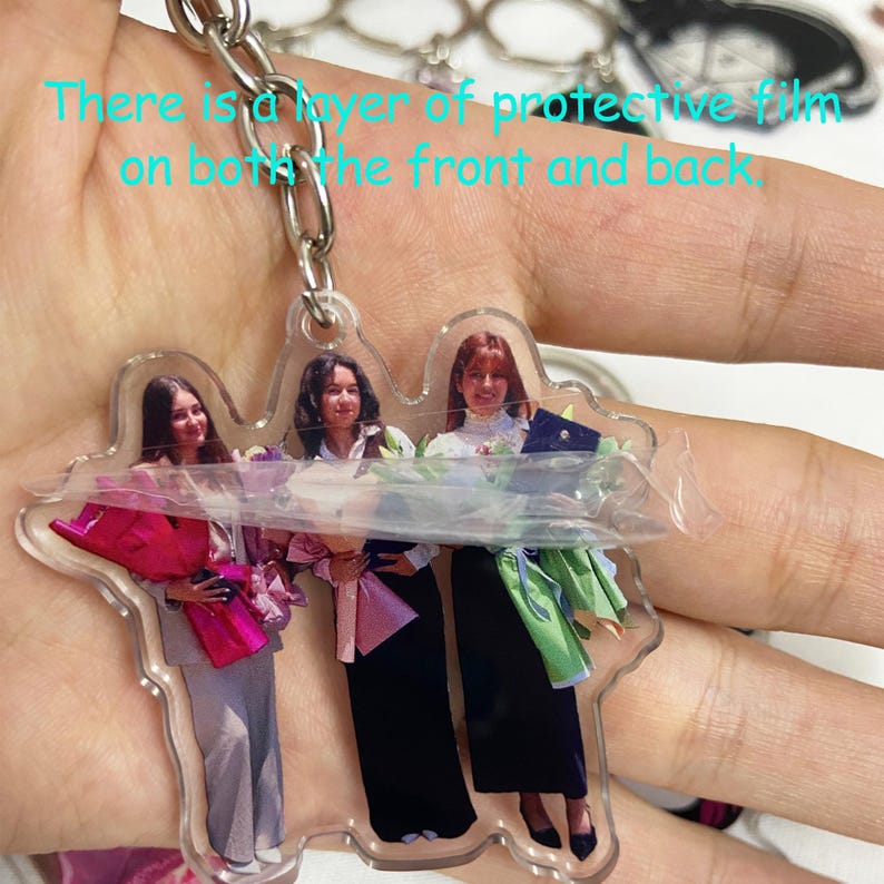 May include: Clear acrylic keychain featuring a photo of three people. The keychain has a silver metal chain and a protective film. The image shows three people holding bouquets and wearing formal attire. The text on the image says, "There is a layer of protective film on both the front and back."