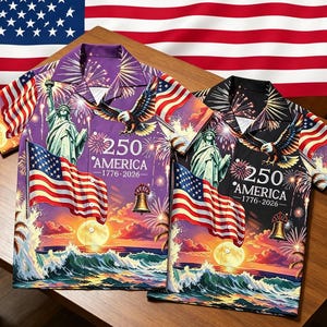 Puede incluir: Dos camisas de manga corta con botones y un estampado gráfico patriótico de la Estatua de la Libertad, un águila calva, la bandera estadounidense, una campana, fuegos artificiales y el texto 250 AMERICA 1776-2026. Una es morada y otra negra.