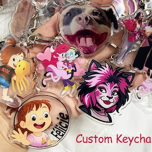 May include: A collection of custom keychains featuring various designs, including cartoon characters, a dog's face, and images of people. The keychains are made of clear acrylic and have silver key rings. The text "Custom Keychain" is visible.