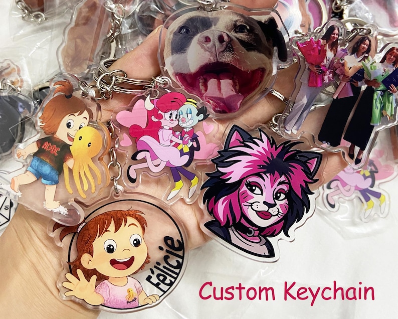 May include: A collection of custom keychains featuring various designs, including cartoon characters, a dog's face, and images of people. The keychains are made of clear acrylic and have silver key rings. The text "Custom Keychain" is visible.