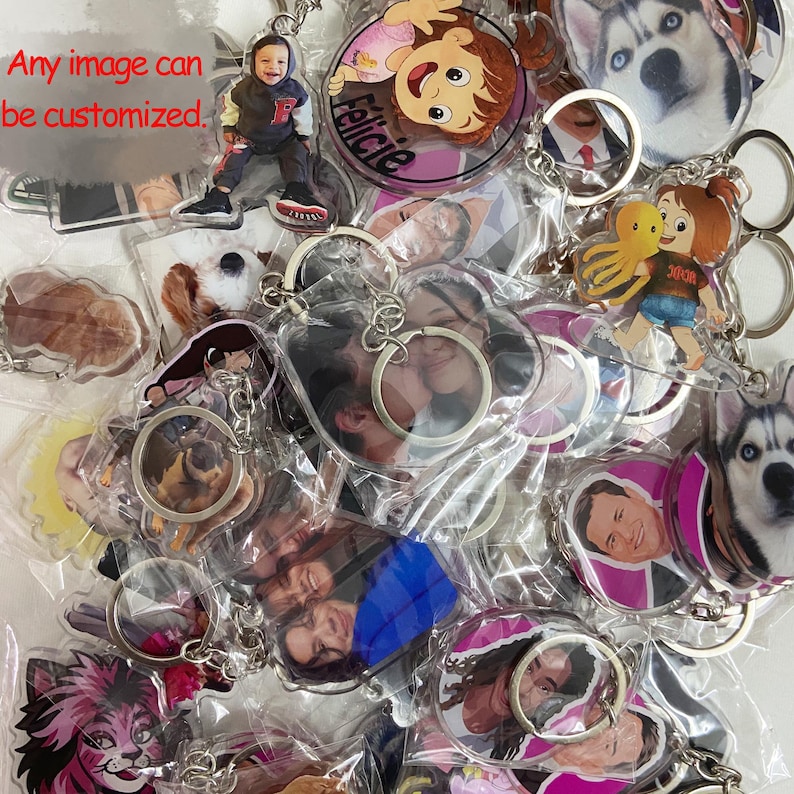 May include: A collection of clear acrylic keychains with various images, including photos of people, cartoon characters, and a dog. The keychains have silver metal rings. Text on the image reads: "Any image can be customized."