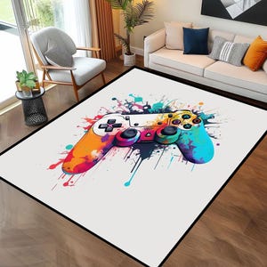 Peut inclure: Un tapis blanc avec un motif de peinture éclaboussée coloré mettant en vedette une grande manette de jeu vidéo noire et blanche. La manette est entourée d'éclaboussures de peinture colorées dans des tons de bleu, vert, jaune, orange, rose et violet.