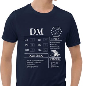 May include: A navy blue t-shirt with a white graphic of a Dungeons and Dragons character sheet. The character sheet includes the text "DM" and stats for Strength, Dexterity, Constitution, Intelligence, Wisdom, and Charisma. The graphic also includes a white dragon.