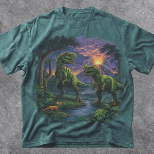 May include: Blue Spruce t-shirt featuring a detailed illustration of two green Tyrannosaurus Rex dinosaurs in a prehistoric landscape with a river, trees, and a volcano. The shirt has the text "Blue Spruce" at the bottom.