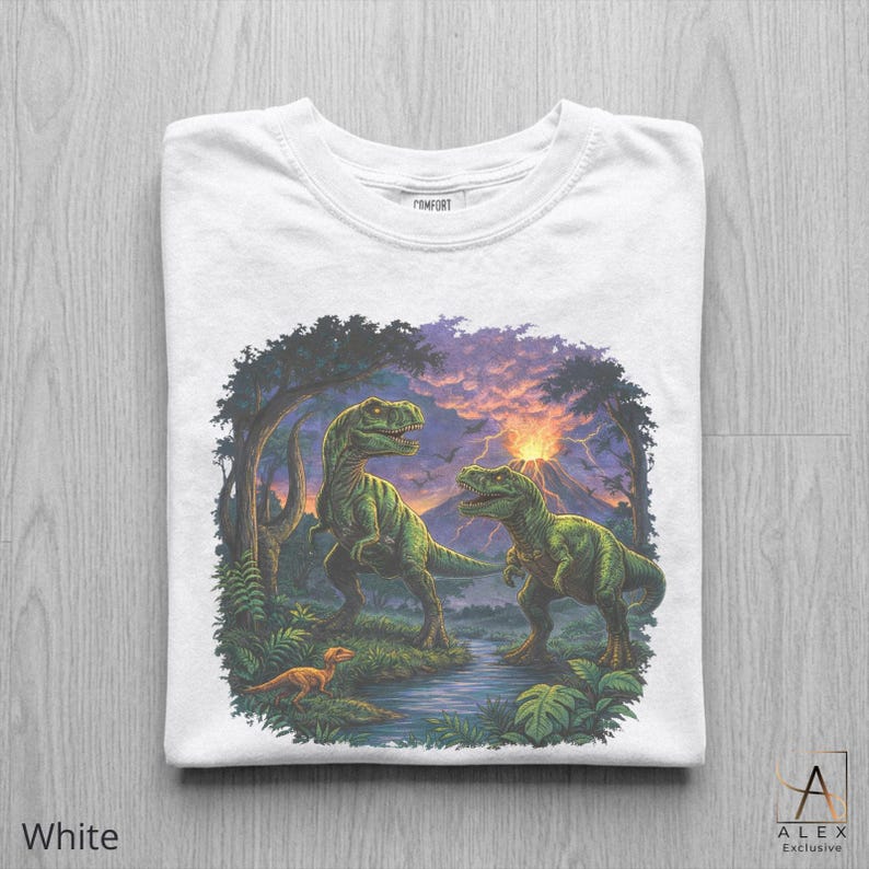 May include: White t-shirt featuring a detailed illustration of two green dinosaurs in a prehistoric landscape with a volcano and a small dinosaur. The shirt has the word "COMFORT" printed on the collar and the words "ALEX Exclusive" on the bottom right.