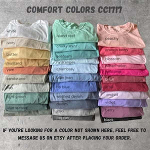 May include: Stacks of Comfort Colors CC1717 t-shirts in various colors, including white, ivory, and peachy. The image displays a range of hues, from light green to black, with each color labeled. Text at the top reads "COMFORT COLORS CC1717".