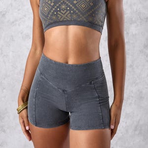 Op de afbeelding: Een antracietgrijze sport-bh en bijpassende shortset. De sport-bh heeft een geometrisch goudkleurig patroon over de borst. De shorts hebben een hoge taille en een getailleerd ontwerp. De set is gemaakt van een zacht, rekbaar materiaal.