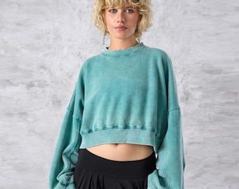 May include: A cropped, long-sleeve sweatshirt in a faded teal green colour. The garment features a crew neckline, dropped shoulders, and wide, voluminous sleeves with ribbed cuffs. The hem is also ribbed and sits above the waistline.