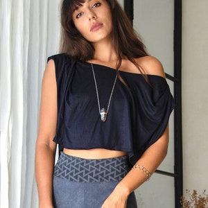 Könnte beinhalten: Eine Frau trägt ein schwarzes, schulterfreies Crop-Top mit einer silbernen Kettenkette und einem Kristallanhänger. Sie trägt auch graue Leggings mit einem geometrischen Muster am Bund und einem goldenen Kettenarmband.