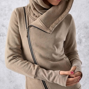 May include: A tan hooded sweatshirt with a diagonal zip and thumbhole cuffs. The sweatshirt features a high, wrap-around collar and a hood. The zip is black, and the fabric appears to be a soft, knitted material. The overall style is casual and modern.