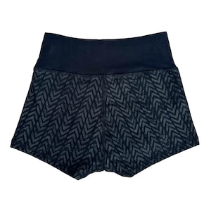 May include: Black athletic shorts with a high waistband. The shorts feature a dark gray chevron pattern on the legs and a solid black waistband. The shorts are designed for athletic activities.