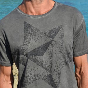 以下が含まれることがあります： 小さな点でできた黒い星のデザインが施されたグレーのTシャツ。星は幾何学的な形をしていて、モダンな雰囲気です。