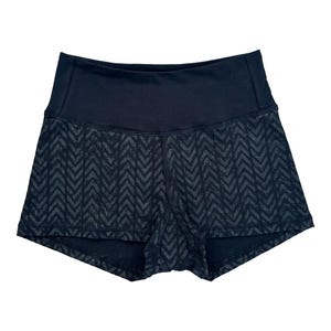 May include: Black athletic shorts with a high waistband. The shorts feature a dark gray chevron pattern on the lower portion. The waistband is solid black. These shorts are designed for fitness activities.