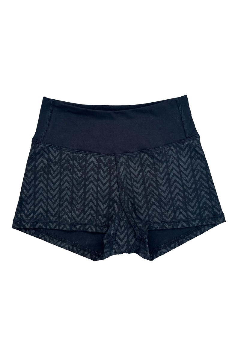 May include: Black athletic shorts with a high waistband. The shorts feature a dark gray chevron pattern on the lower portion. The waistband is solid black. These shorts are designed for fitness activities.