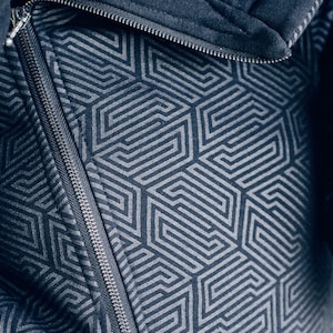 May include: A close-up of a dark blue zipper on a jacket with a geometric pattern. The zipper is silver and has a black pull tab.