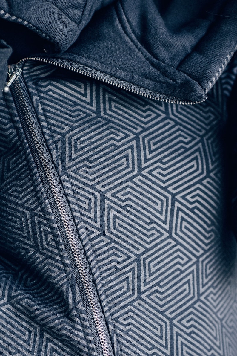 May include: A close-up of a dark blue zipper on a jacket with a geometric pattern. The zipper is silver and has a black pull tab.