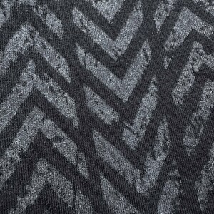 May include: Close-up of a black fabric with a repeating chevron pattern in shades of gray. The design has a textured, distressed appearance, creating a visual contrast between the dark background and the lighter pattern.
