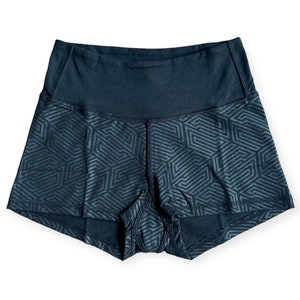 May include: Dark blue athletic shorts with a geometric pattern. The shorts have a high waistband and a repeating design of interlocking shapes. The fabric appears to be a moisture-wicking material, suitable for workouts or athletic activities.