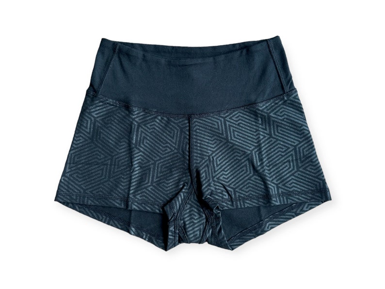 May include: Dark blue athletic shorts with a geometric pattern. The shorts have a high waistband and a repeating design of interlocking shapes. The fabric appears to be a moisture-wicking material, suitable for workouts or athletic activities.