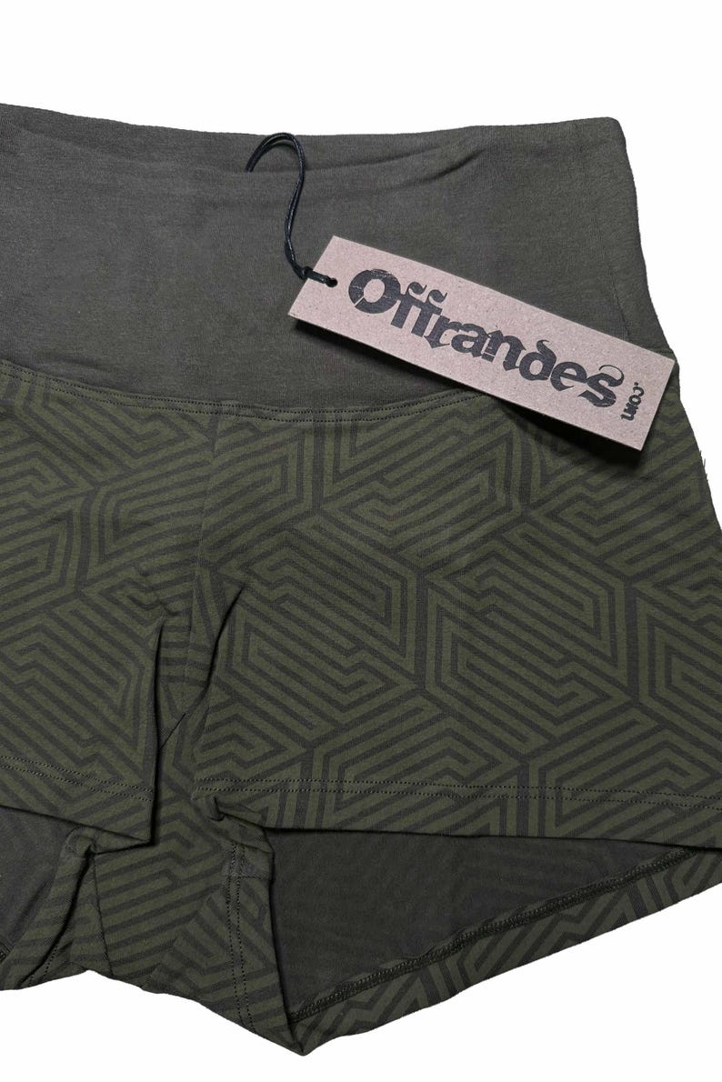 May include: Olive green athletic shorts with a geometric pattern in a darker shade of green. The shorts have a high waistband and a tag that reads "Offrandes".