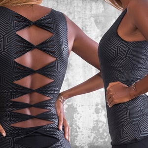 Puede incluir: Top negro sin mangas con un patrón geométrico. La espalda presenta un diseño entrecruzado con detalles recortados. El top es entallado y está hecho de una tela brillante y texturizada. El estilo general es moderno y atrevido.