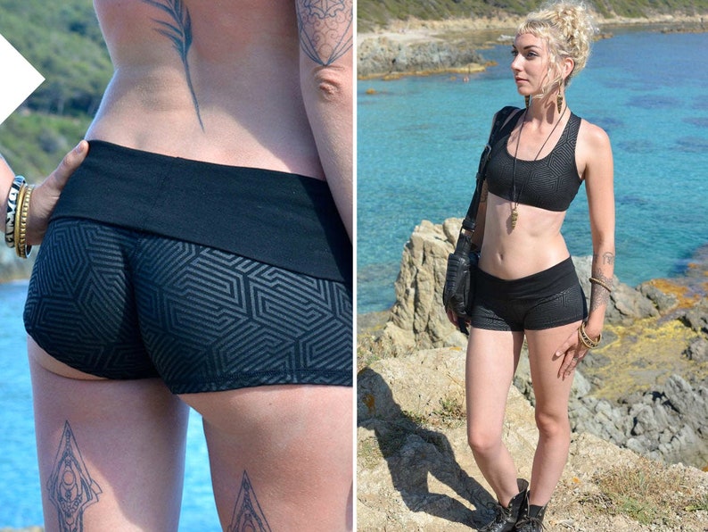 May include: Black athletic shorts and matching sports bra with a geometric pattern. The shorts have a wide waistband. The bra has a scoop neck. The model is standing on a rocky cliff near the ocean.