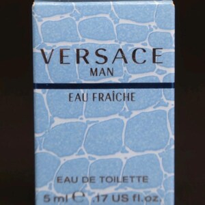 Puede incluir: Caja rectangular de Eau de Toilette Versace Man Eau Fra&icirc;che. La caja es azul claro con un patr&oacute;n que se asemeja al agua. El texto "VERSACE MAN" es dorado. Contiene 5 ml.