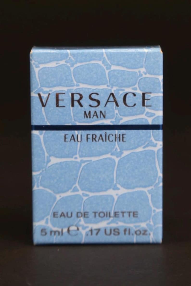 Puede incluir: Caja rectangular de Eau de Toilette Versace Man Eau Fra&icirc;che. La caja es azul claro con un patr&oacute;n que se asemeja al agua. El texto "VERSACE MAN" es dorado. Contiene 5 ml.