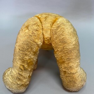 May include: A vintage plush toy in the shape of a dog, with a light brown fur and a worn appearance. The toy is sitting on its hind legs, with its front legs extended forward.