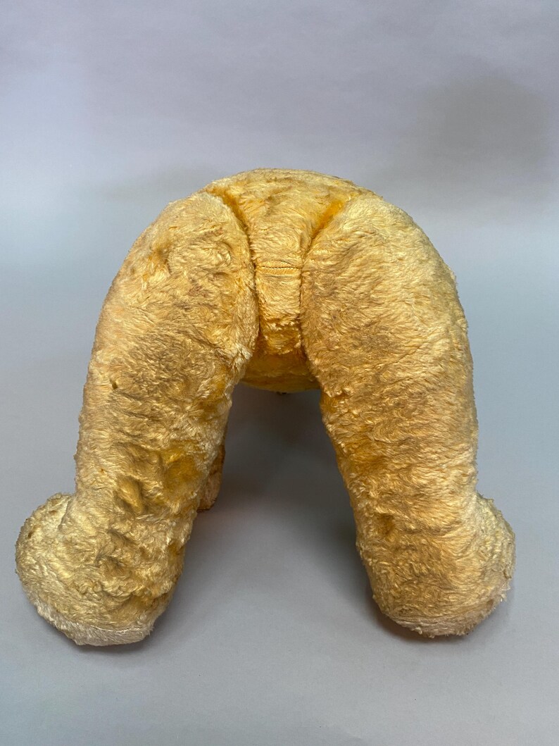 May include: A vintage plush toy in the shape of a dog, with a light brown fur and a worn appearance. The toy is sitting on its hind legs, with its front legs extended forward.