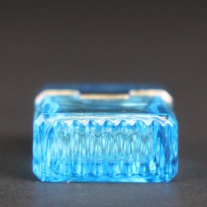 Puede incluir: Una caja de baratijas rectangular de vidrio azul claro con un dise&ntilde;o acanalado texturizado en los lados. La caja tiene una apariencia clara y transparente y se encuentra sobre un fondo oscuro. La caja probablemente se utiliza para guardar objetos peque&ntilde;os.