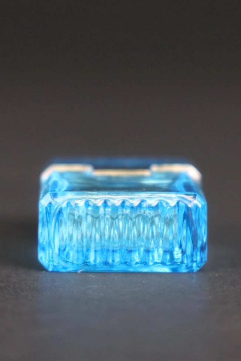 Puede incluir: Una caja de baratijas rectangular de vidrio azul claro con un dise&ntilde;o acanalado texturizado en los lados. La caja tiene una apariencia clara y transparente y se encuentra sobre un fondo oscuro. La caja probablemente se utiliza para guardar objetos peque&ntilde;os.