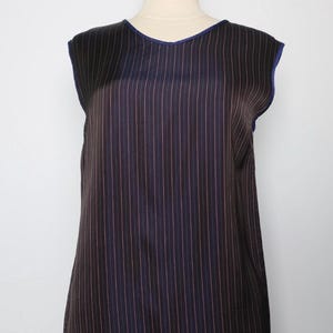 May include: Sleeveless top featuring vertical stripes in brown, black, and pink. The top has a rounded neckline and blue trim. The garment is displayed on a mannequin, highlighting its design and fit. A stylish addition to any wardrobe.