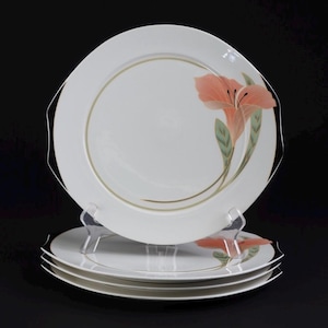 May include: A stack of white ceramic dinner plates featuring a subtle gold circular rim and a delicate peach-coloured lily illustration with green leaves on the right side. The plates have a slightly octagonal edge design and a smooth finish.