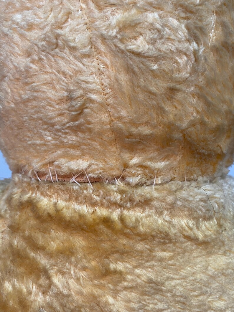 May include: Close-up of the back seam of a light brown plush toy. The seam is stitched with a light brown thread.