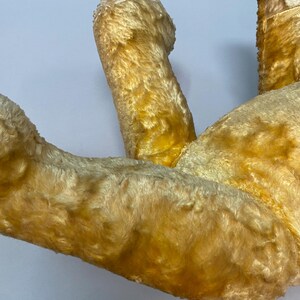 May include: A vintage, yellow plush teddy bear with a worn, faded appearance. The bear is lying on its back with its legs in the air.