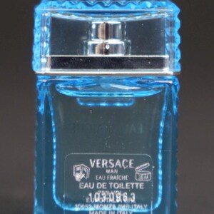 Puede incluir: Peque&ntilde;a botella rectangular de Versace Man Eau Fraiche Eau de Toilette. La botella de vidrio azul transparente tiene un atomizador plateado y una tapa azul claro texturizada. La etiqueta incluye el nombre de la marca y detalles del producto.