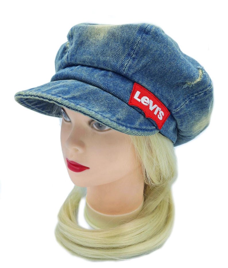 May include: A blue denim cap with a short brim. The cap has a red Levi's logo patch on the side. The denim has a faded, worn look. The cap is on a mannequin head with blonde hair and red lipstick.