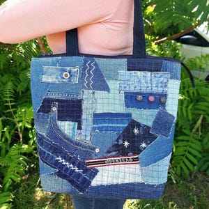May include: A patchwork tote bag constructed from various shades of blue denim fabric. The bag features visible stitching, multiple denim pockets, metal buttons, and a horizontal fabric label with the text OVERZEAS in white lettering.